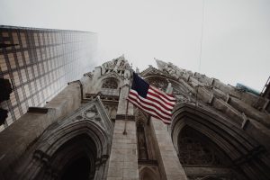 Low angle photography of waving USA flag on brown concrete cathedral